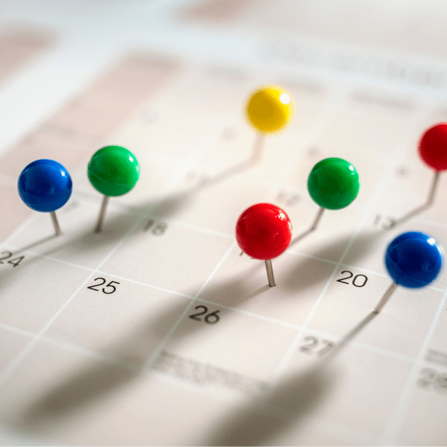 Multi-coloured thumbtacks stuck in various dates on a calendar