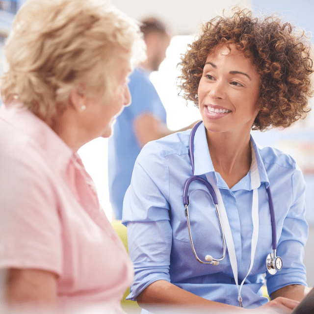 Healthcare provider wearing a stethoscope, sitting and speaking to an elder woman