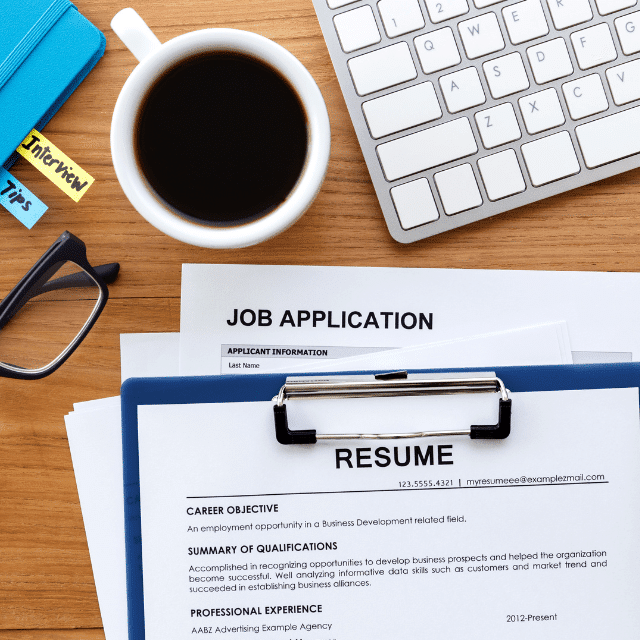 Flat lay of resume and job application on a desk with a cup of coffee, computer keyboard, coffee in a mug, and notebook