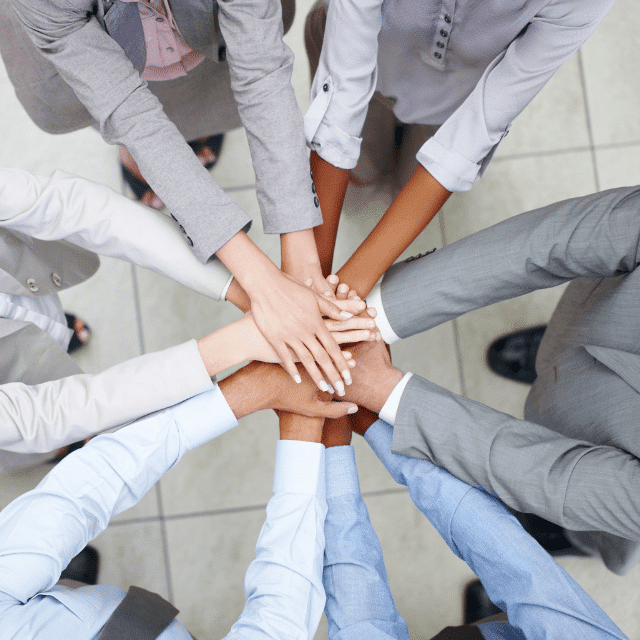 Several people in business attired with their hands together forming a circle