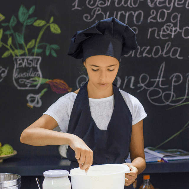 Young woman in black chefs hat and apron stirring ingredients in a bowl