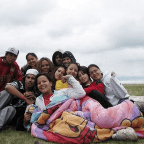 Group of people sitting together on the grass with the front woman under a blanket