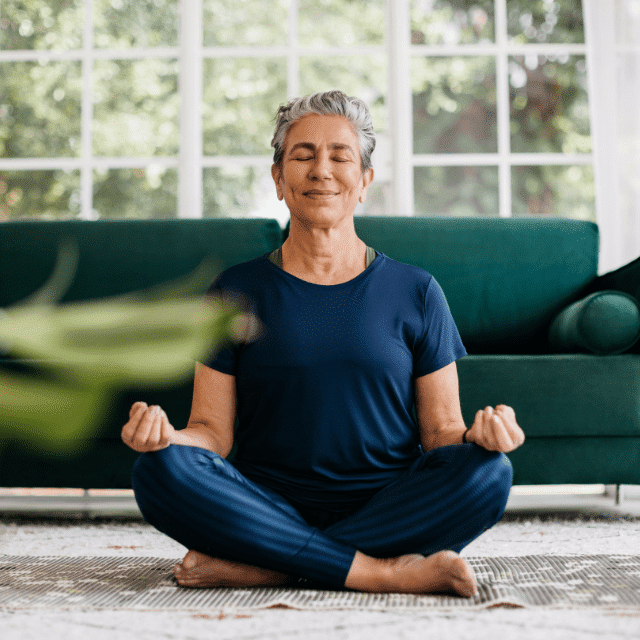 Woman in a seated yoga pose with a green couch and window in the background