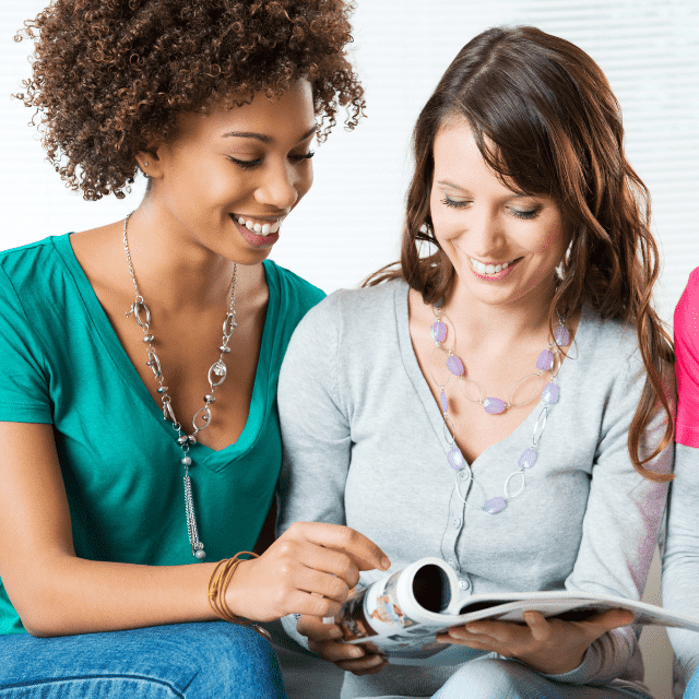 Two women smiling while they look at a magazine together