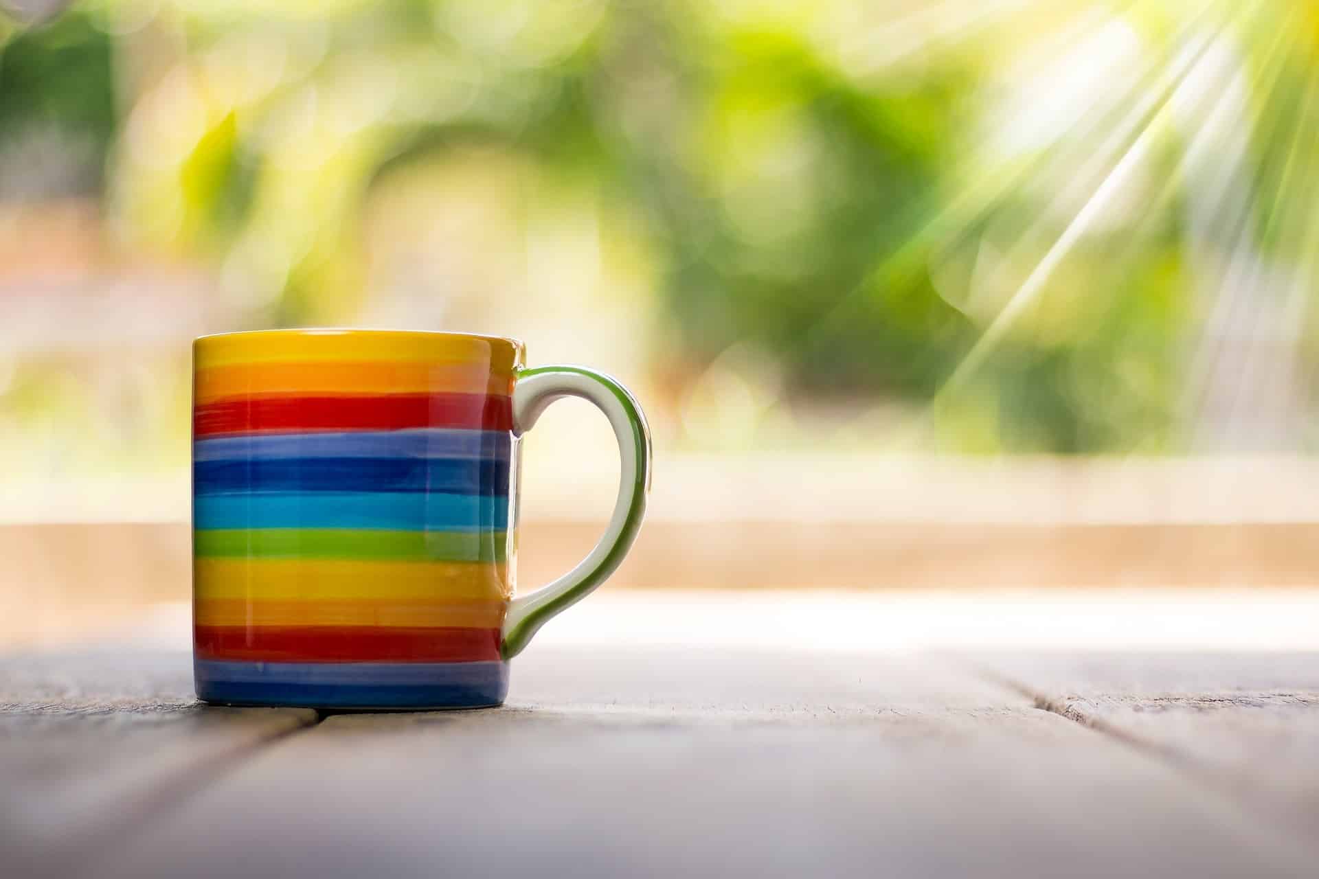 A rainbow painted coffee mug sitting in the sunlight.