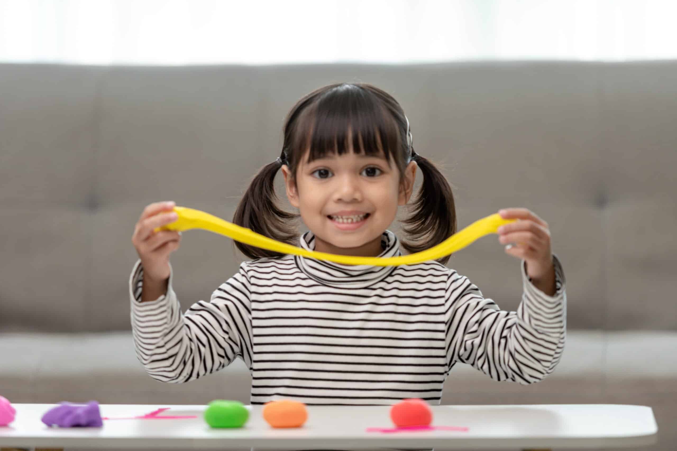 A young girl plays with playdough at a table.