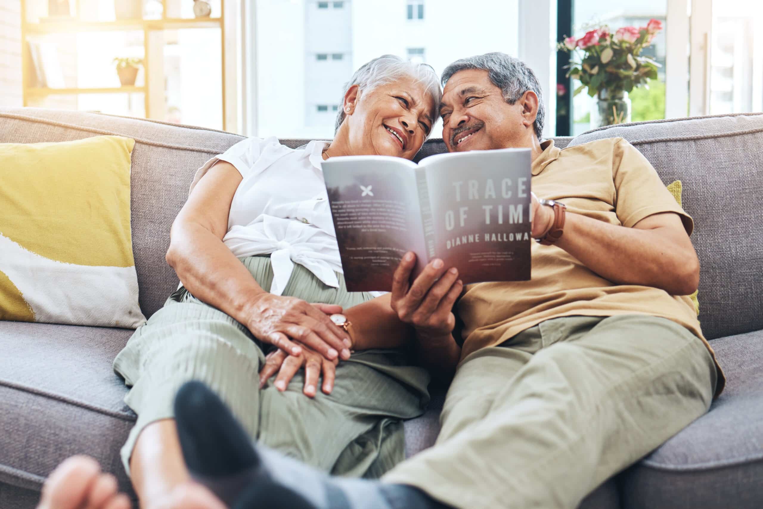 An elderly couple reads together on the couch.