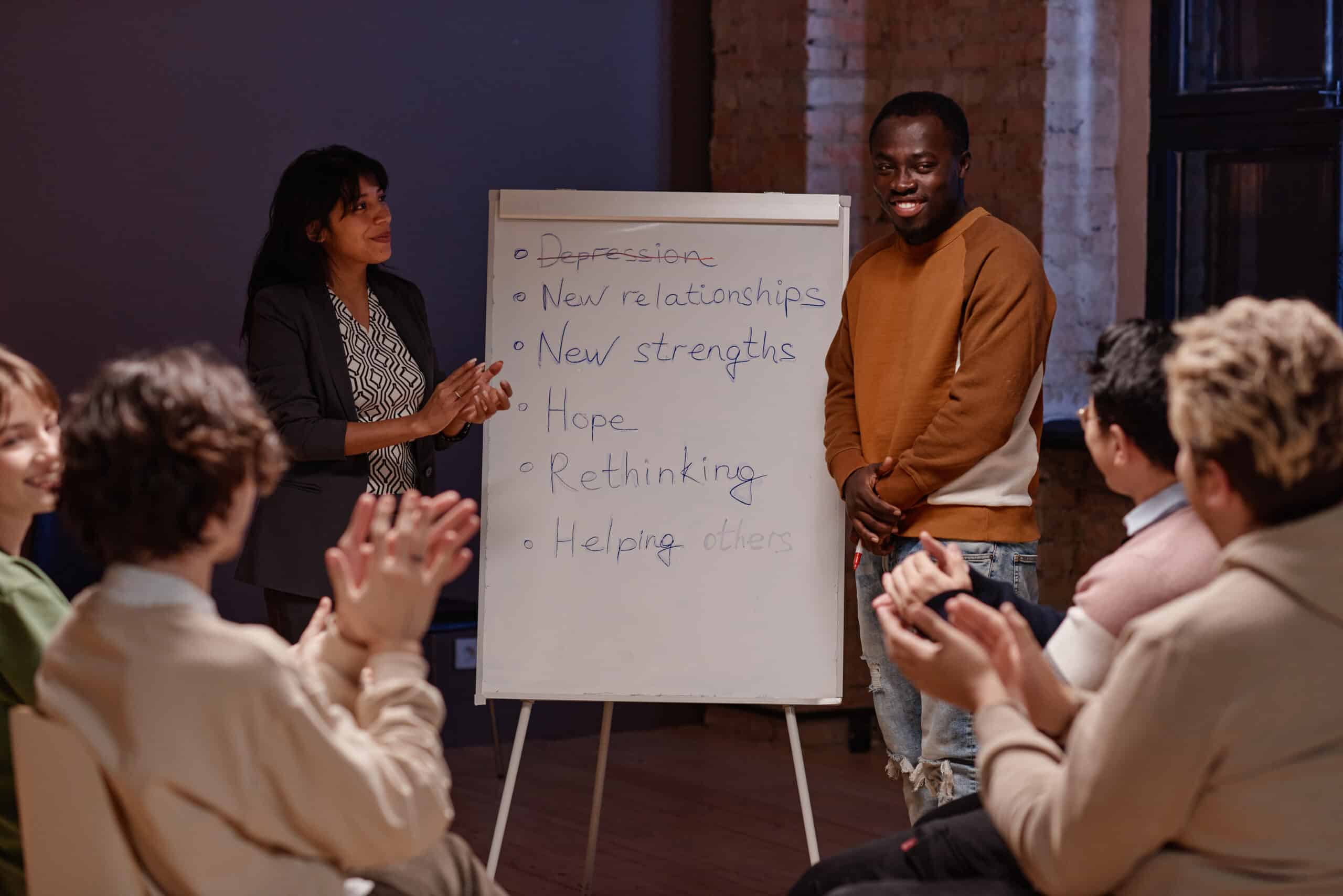 Horizontal shot of people clapping hands to joyful Black man successfully finishing depression treatment with help of group therapy.