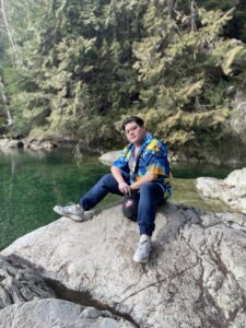 A Photo of Ace sitting on a rock near a body of water.