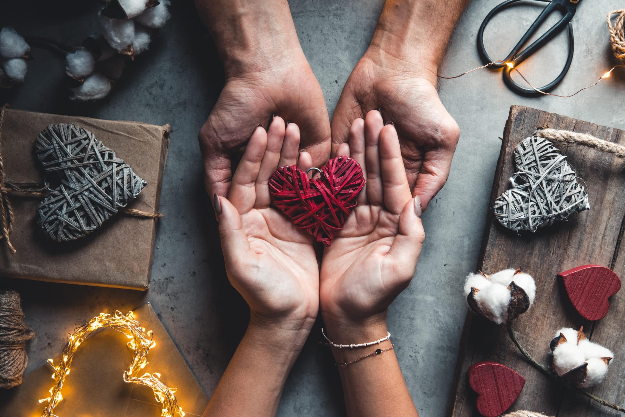 Top view of male and female hands holding red wicker heart used to promote Healing Hearts