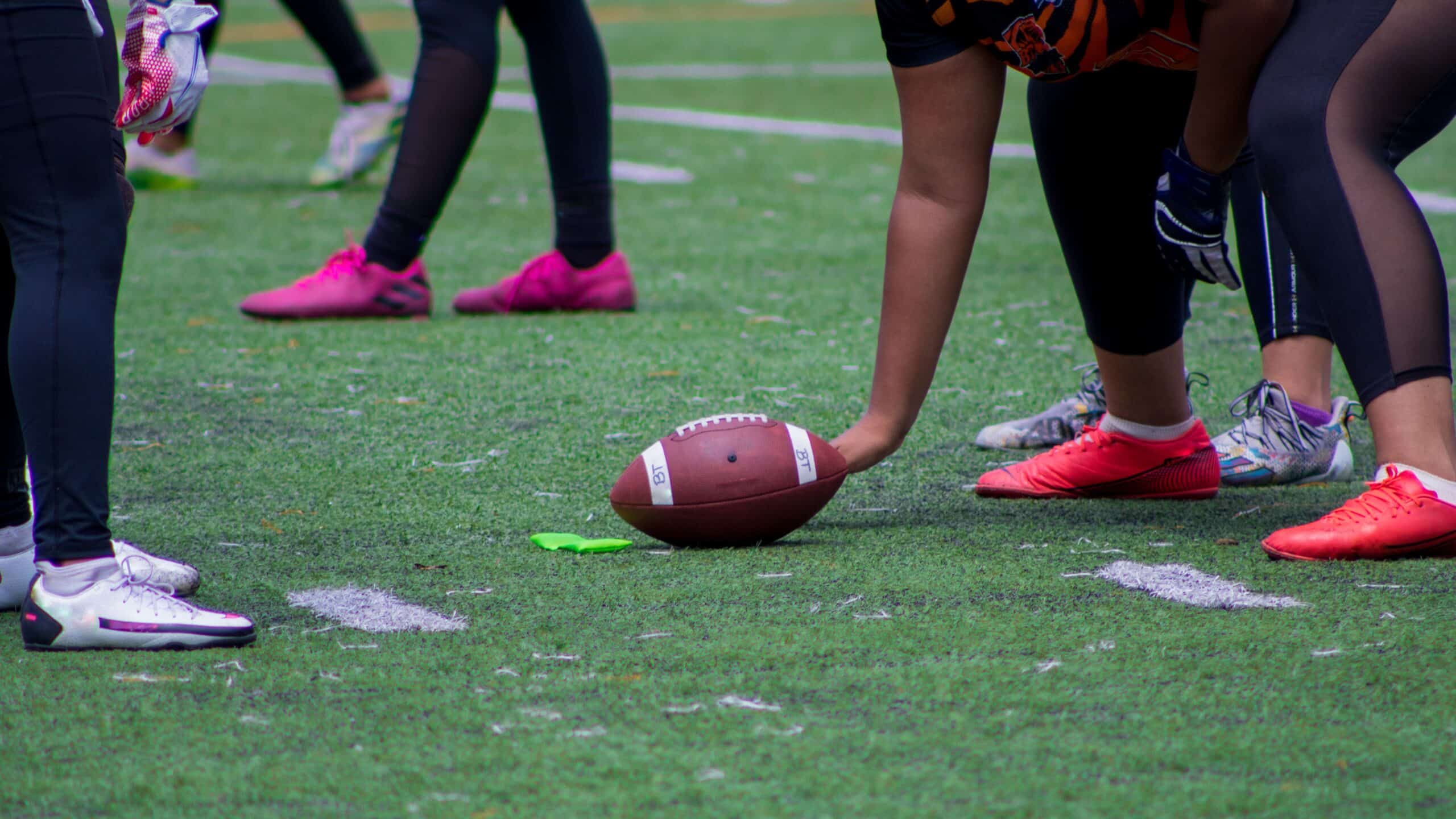 A closeup shot of an American football ball between players hands during a match on a green field