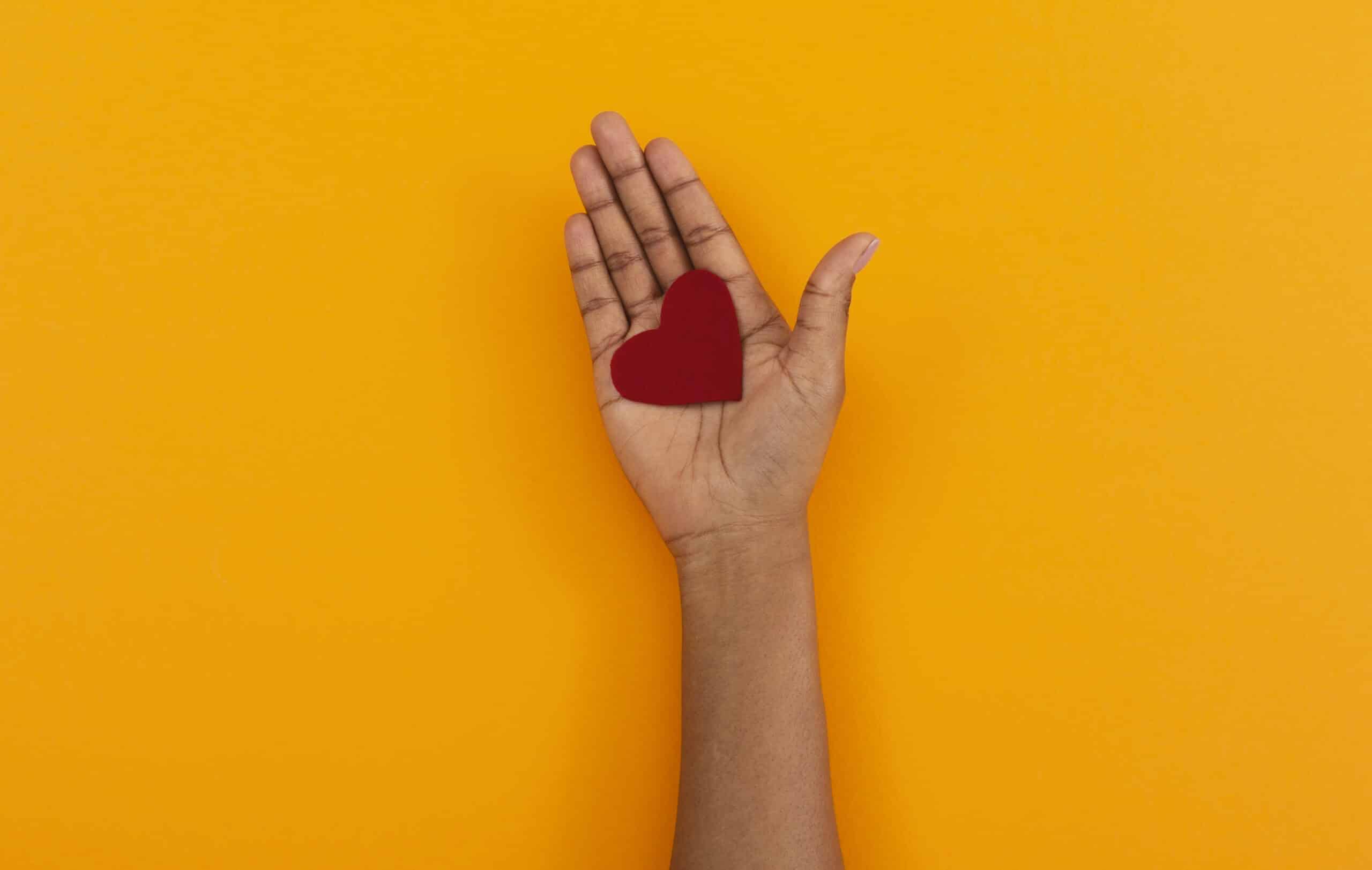Red felt heart in opened palm of african american woman over orange studio background. Used to promote Caring without Crashing