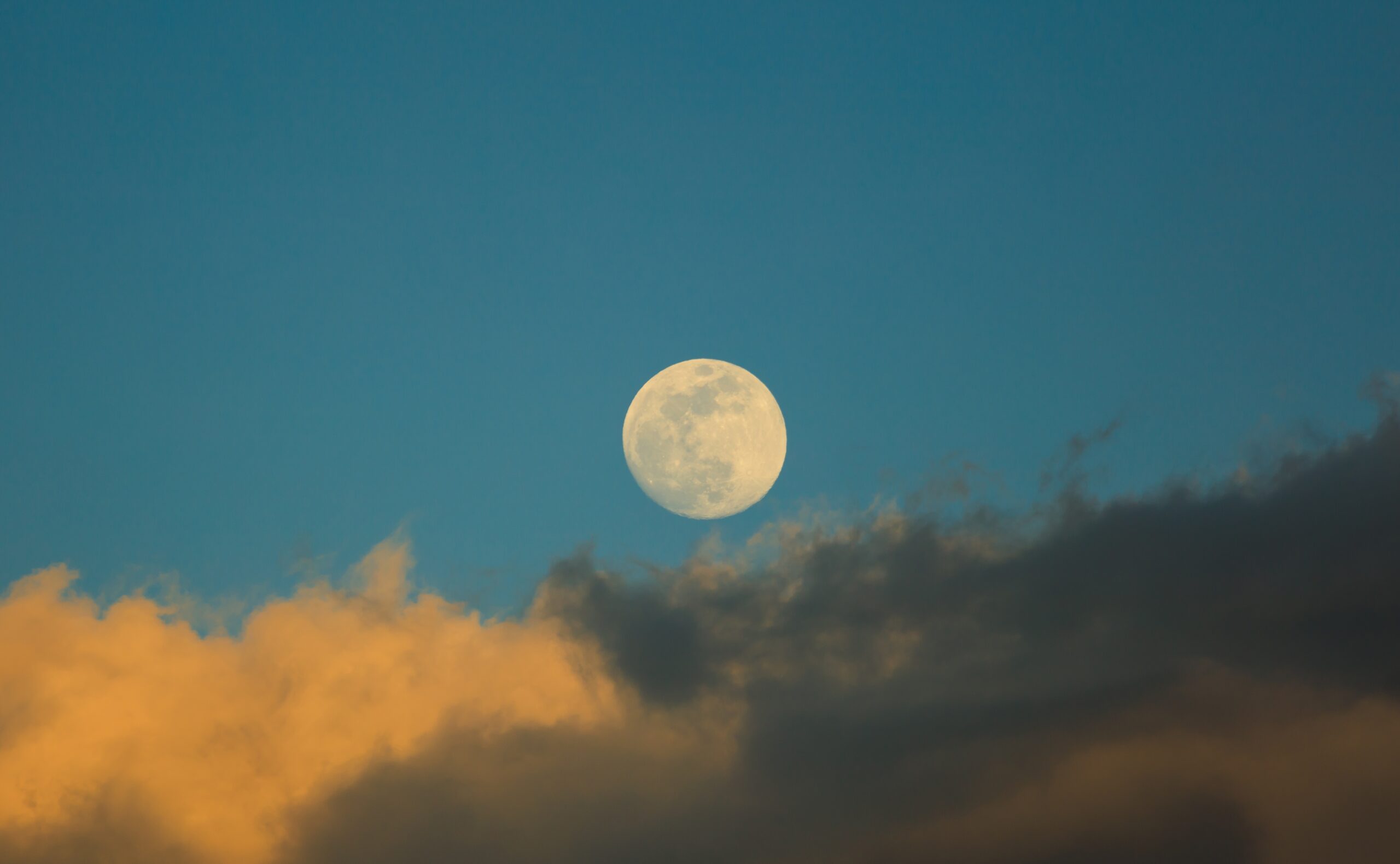 Raspberry Moon in blue sky with grey clouds on foreground