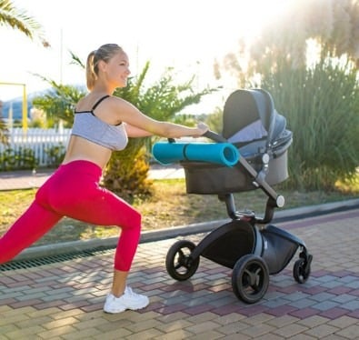 A woman stretches with her stroller in a park