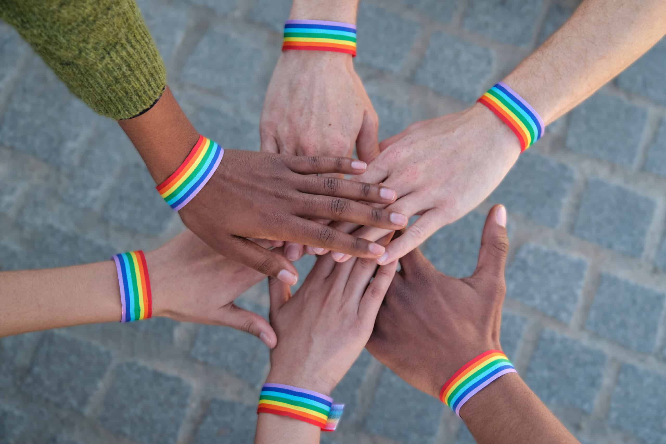 Hands of diverse activists joining together, wearing rainbow wristbands, symbolizing unity and support for LGBTQ plus rights and equality