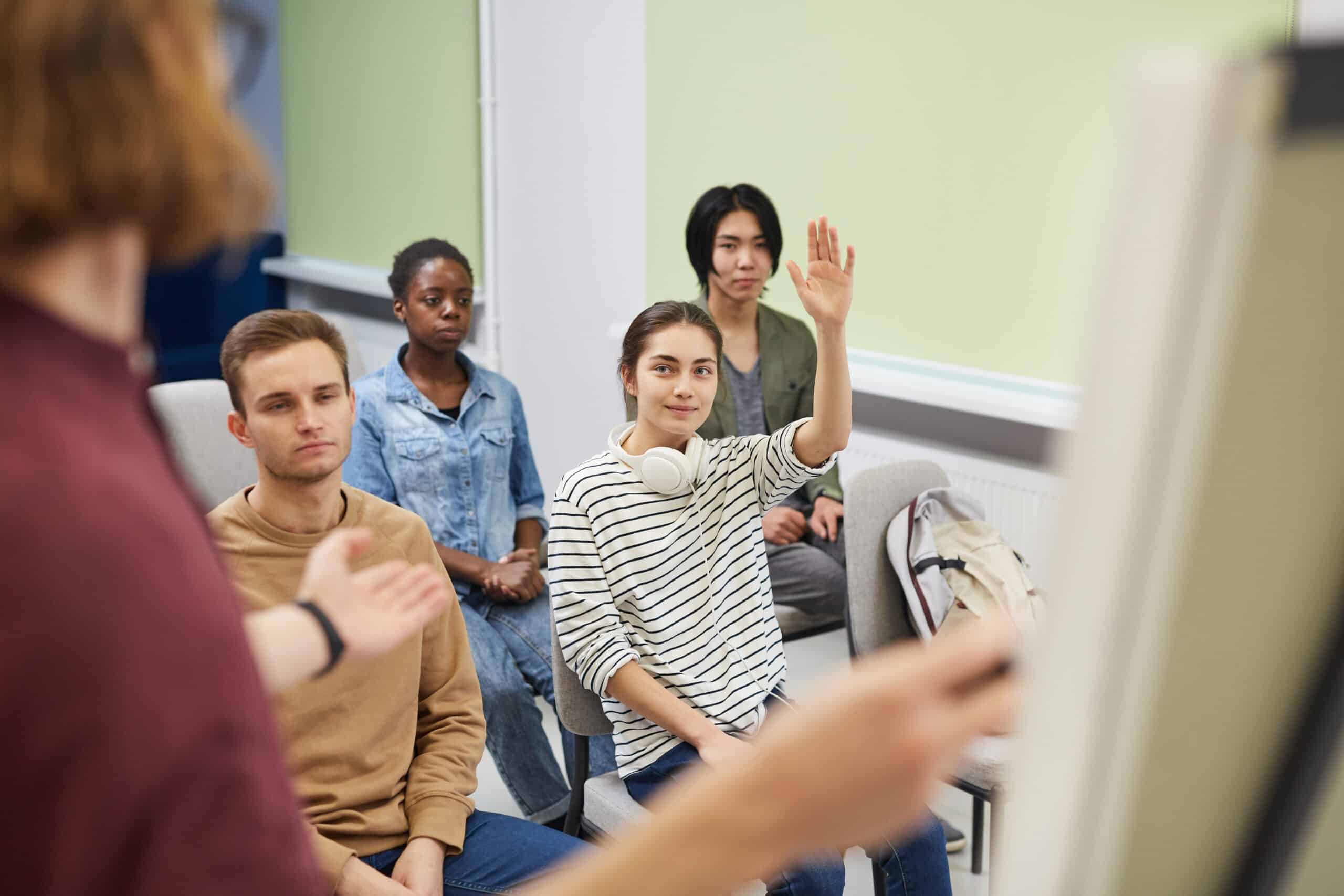 Group of young people sitting and listening to young man who standing pointing at whiteboard and talking to them