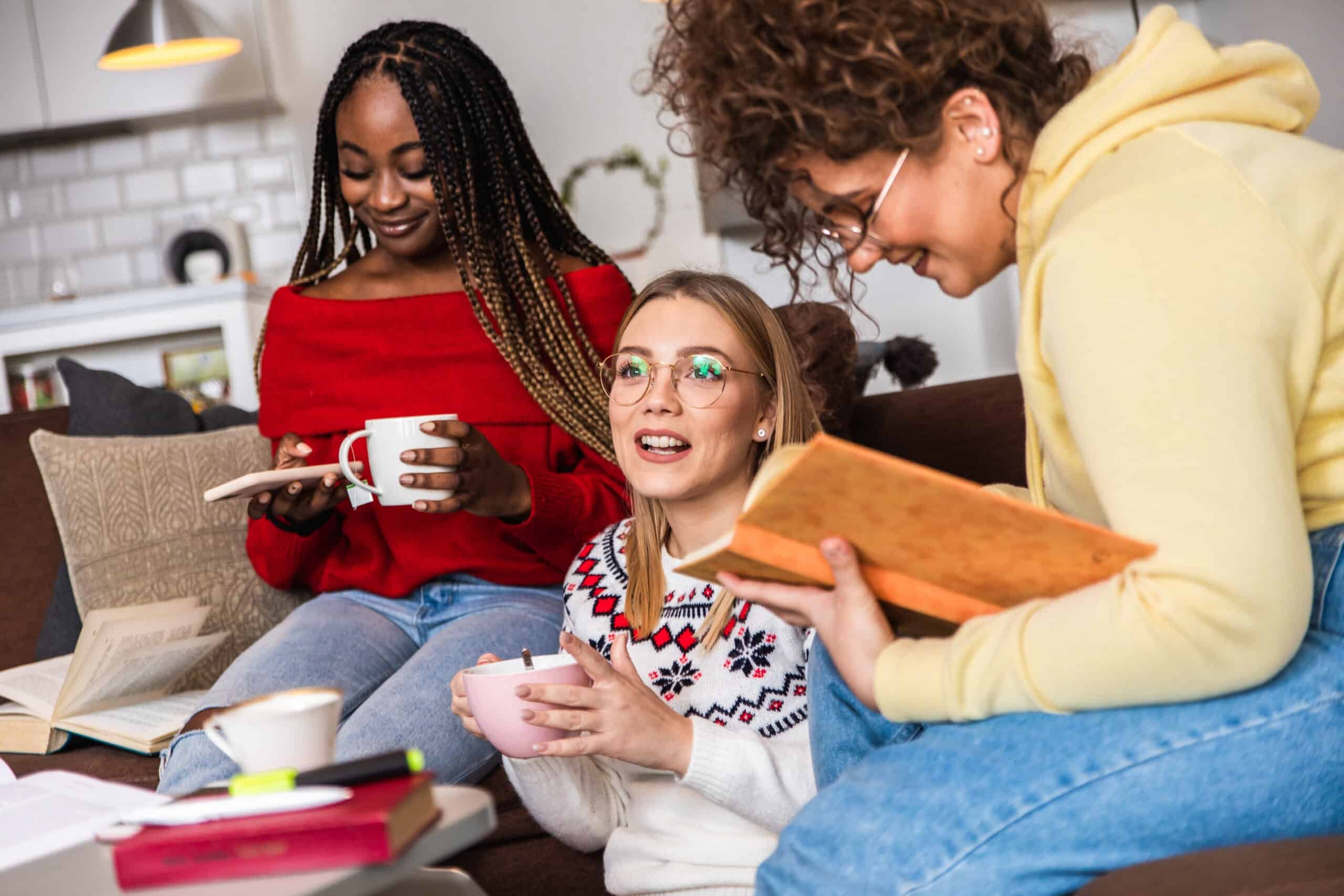 Diverse group female students learning at home using laptop and books for research.
